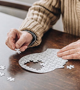 Pessoa idosa sentada à mesa exercita o cérebro completando um puzzle  